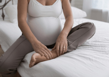 the Pregnant female sits on the bed touch, massages her swollen foot